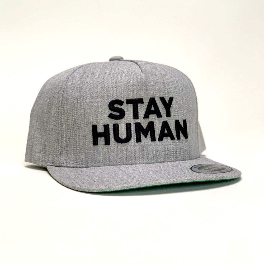 Gray baseball cap with ’STAY HUMAN’ embroidered in black letters on the front.
